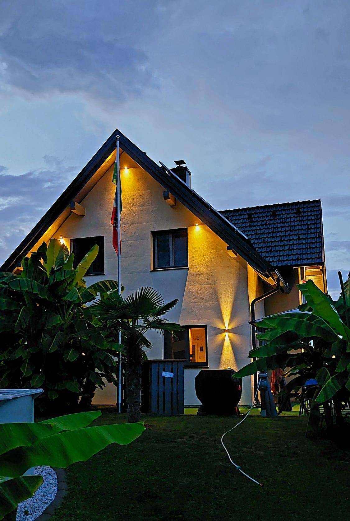 Das Haus in der Abenddämmerung, umgeben von tropischen Pflanzen und stimmungsvoller Beleuchtung.