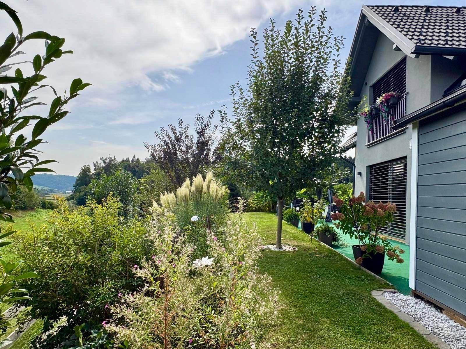 Seitenansicht des Hauses mit blühendem Garten und weitem Blick in die Landschaft.