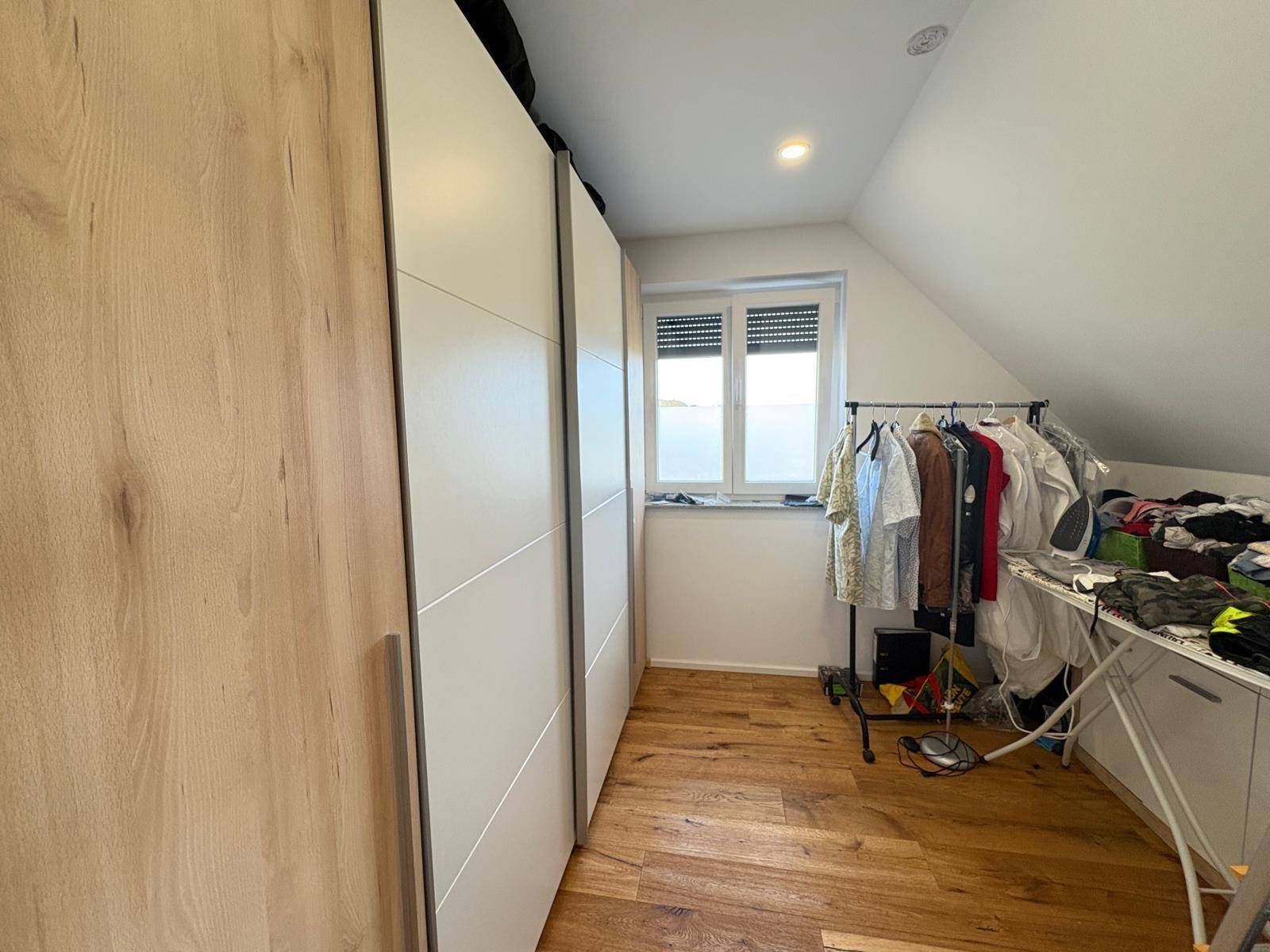 Begehbarer Kleiderschrank mit Einbauschränken und Fenster unter der Dachschräge.
