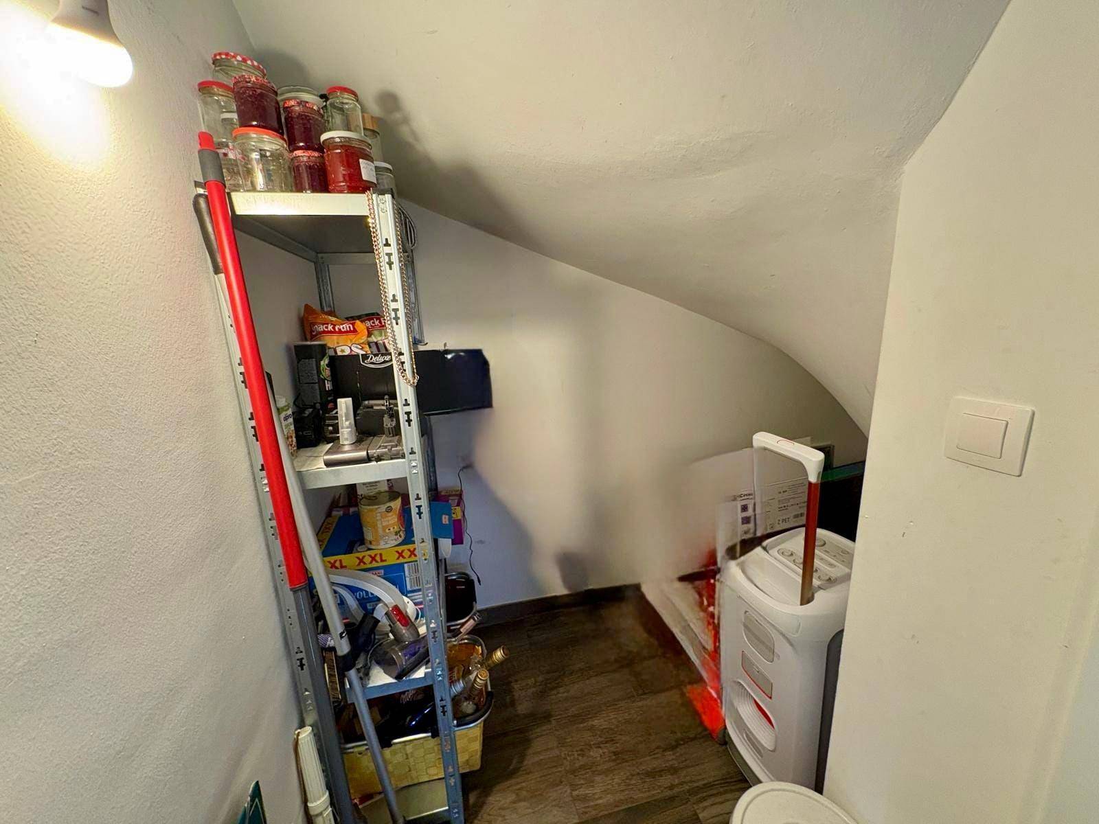 Kleiner Abstellraum unter der Treppe mit Regalen für Vorräte und Haushaltsgeräte.