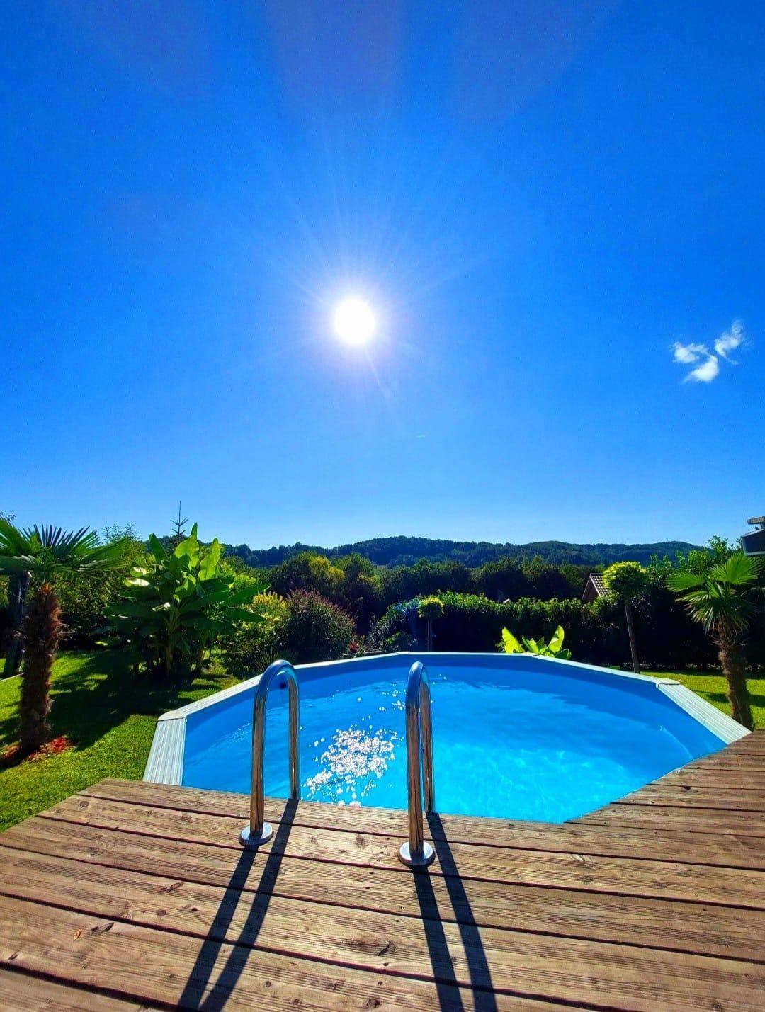 Sonniger Poolbereich mit Holzdeck und weitem Blick über die grüne Hügellandschaft.