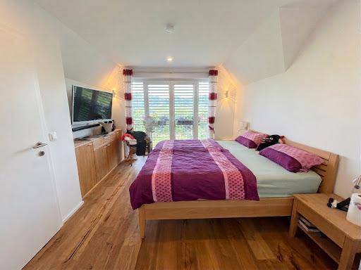 Geräumiges Schlafzimmer mit Holzboden, Fernseher und Schränken unter der Dachschräge.