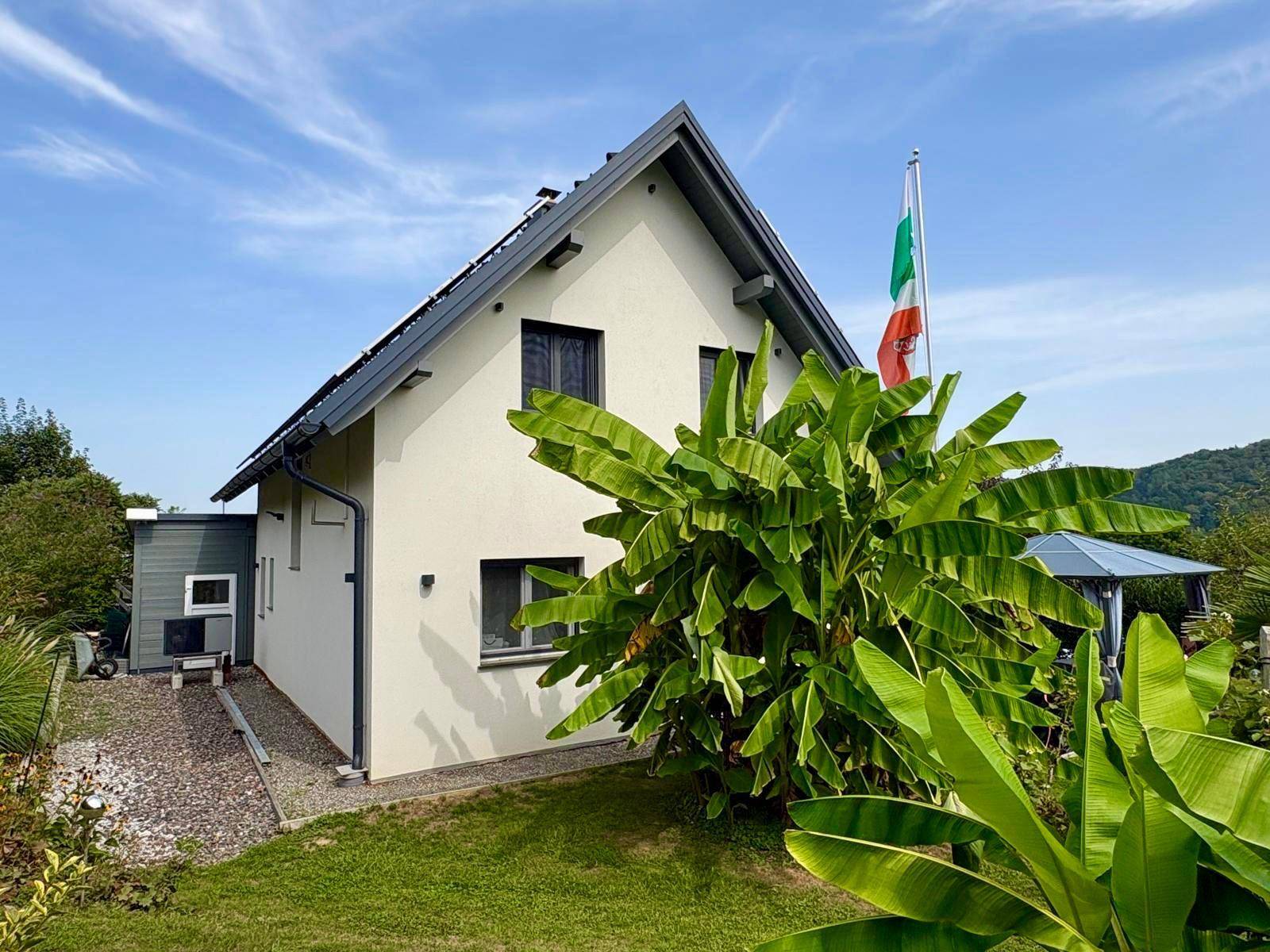 Seitenansicht des Hauses mit üppigen tropischen Pflanzen und einem Pavillon im Hintergrund.