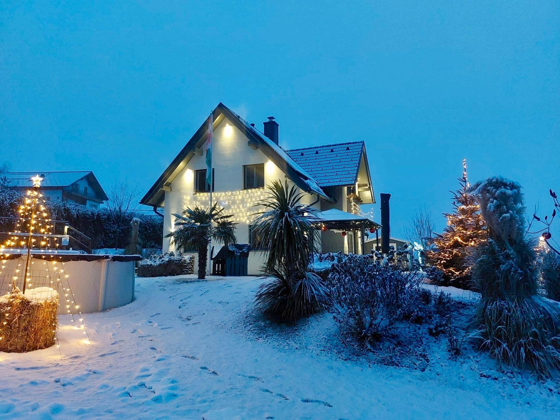 Winterliche Ansicht des Hauses mit verschneitem Garten, beleuchteten Bäumen und einem Pool.