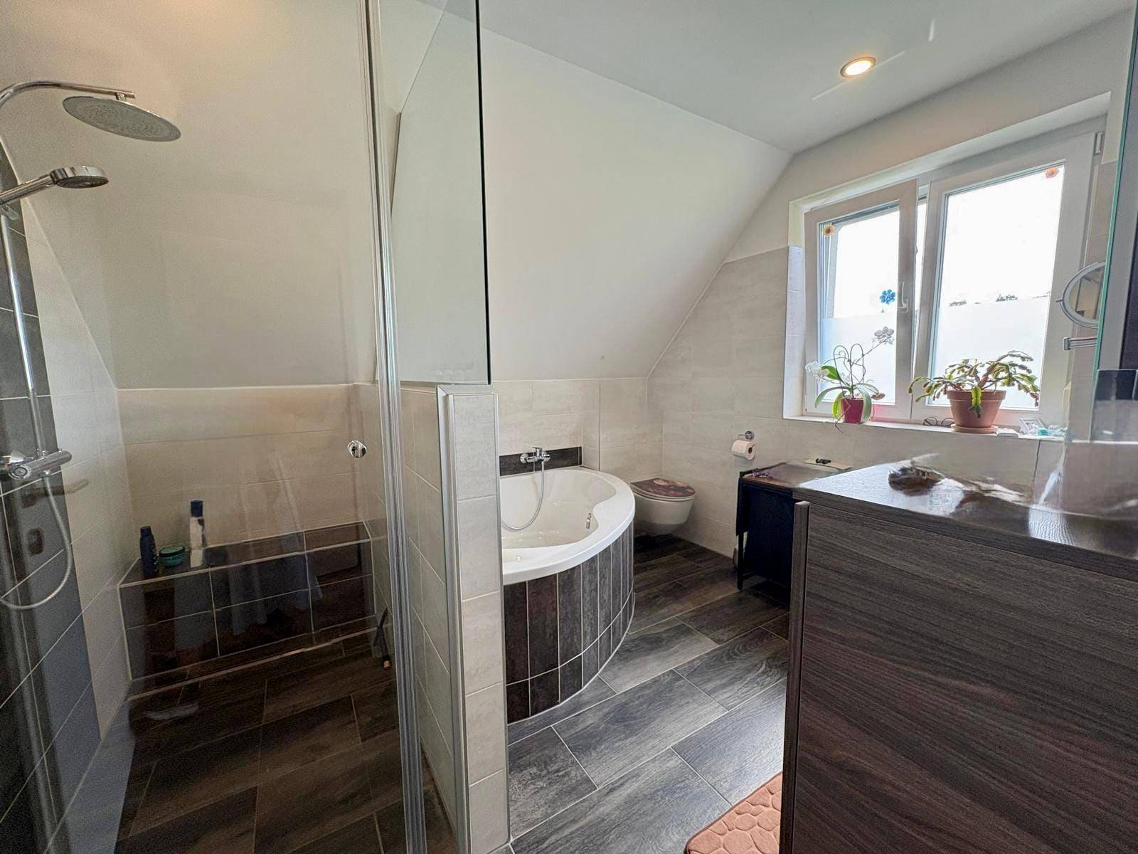 Helles Badezimmer mit Eckbadewanne, Dusche und Dachschräge, gut beleuchtet.