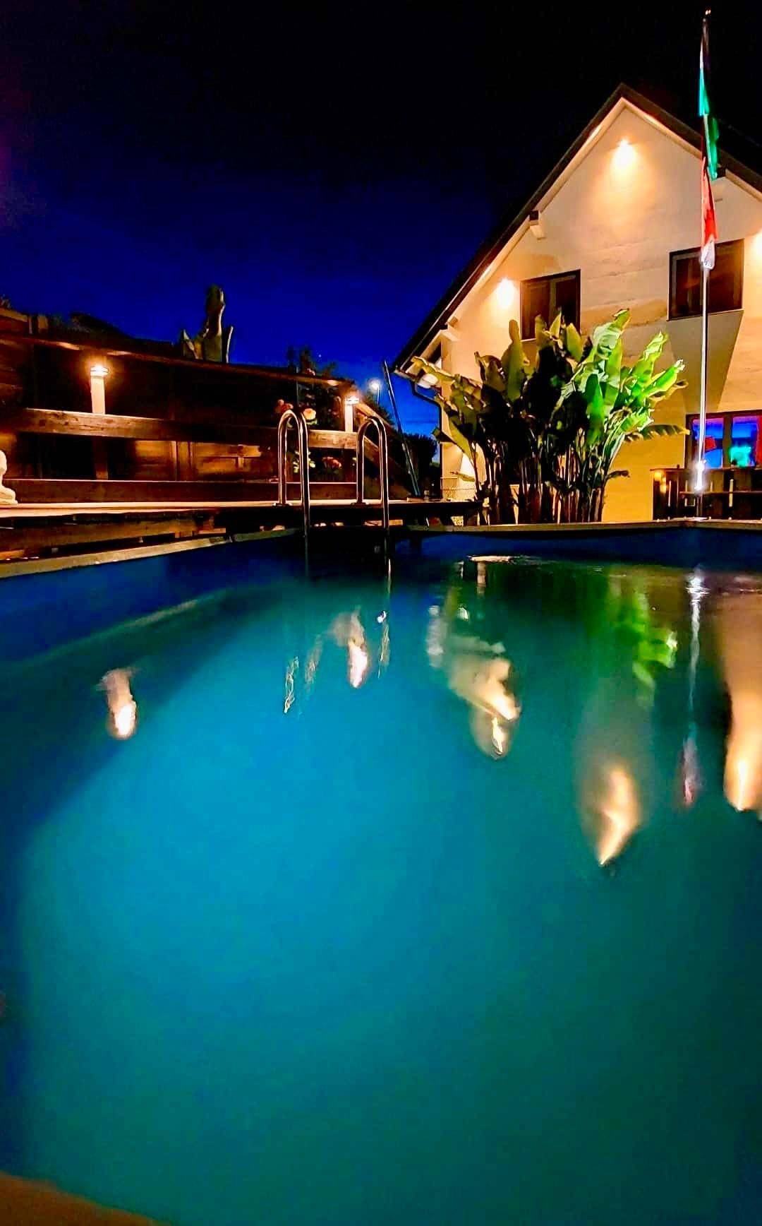 Beleuchteter Poolbereich bei Nacht mit dem Haus im Hintergrund und dunklem Himmel.