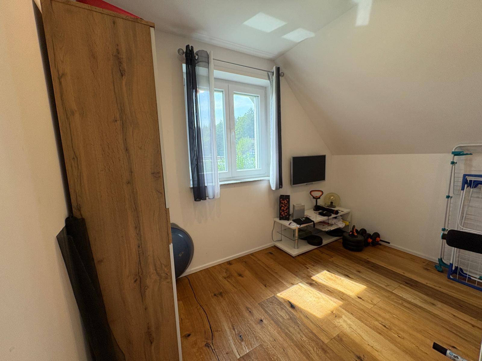 Helles Zimmer mit Holzboden, Fenster und Dachschräge, derzeit als Sportraum genutzt.