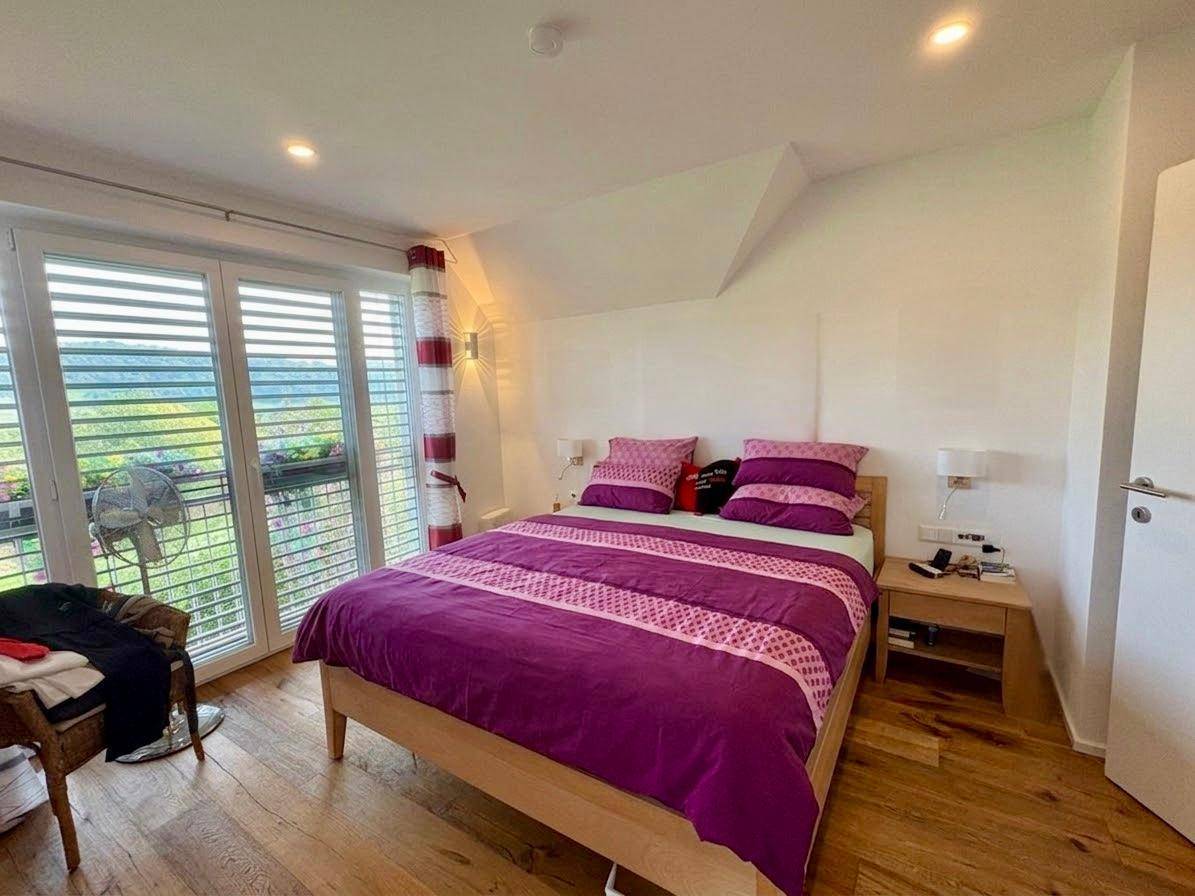 Helles Schlafzimmer mit Doppelbett, Holzboden und Zugang zum Balkon mit Weitblick.