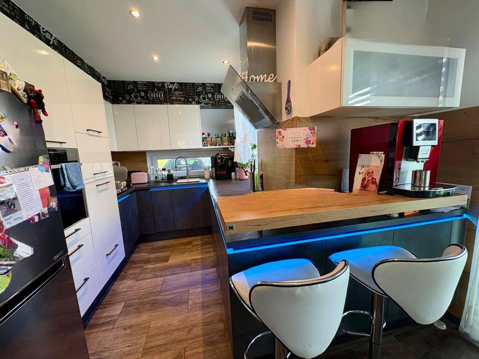 Moderne Küche mit weißen und grauen Schränken, Holztheke und blauer LED-Beleuchtung.