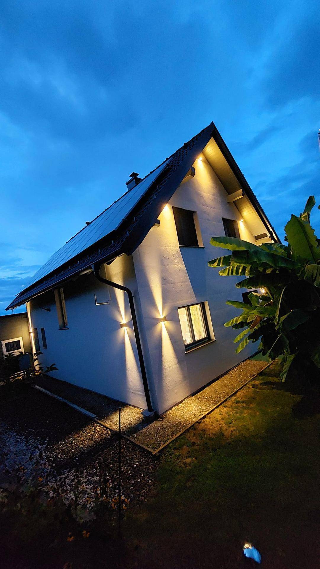 Seitenansicht des Hauses bei Nacht mit akzentuierter Fassadenbeleuchtung und dunklem Himmel.