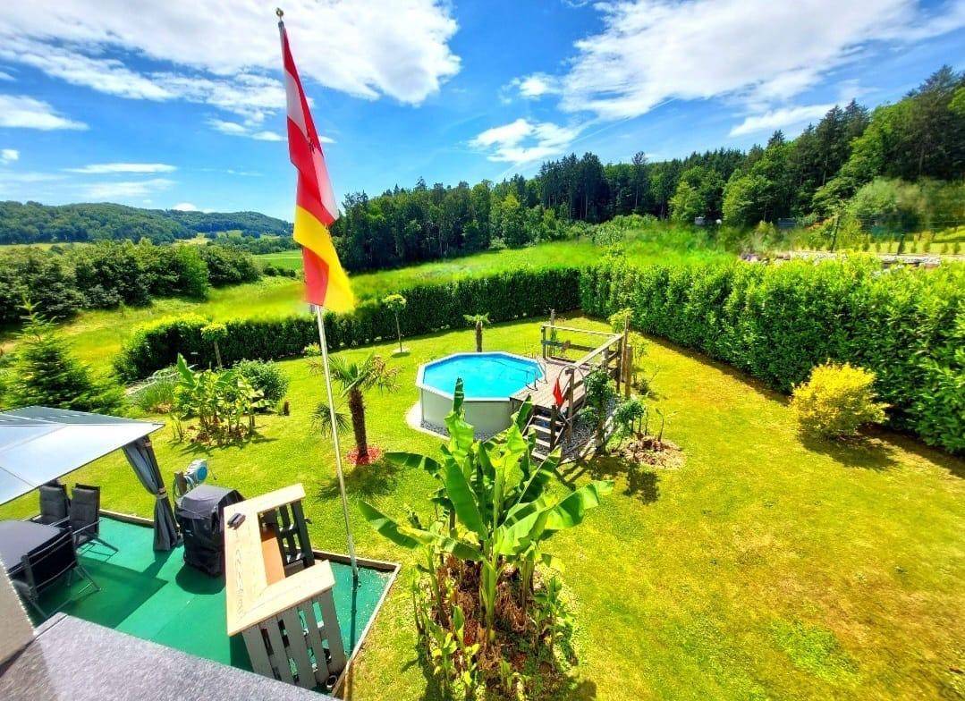 Weitläufiger Garten mit Pool, Holzdeck und Panoramablick auf die umliegende grüne Landschaft.