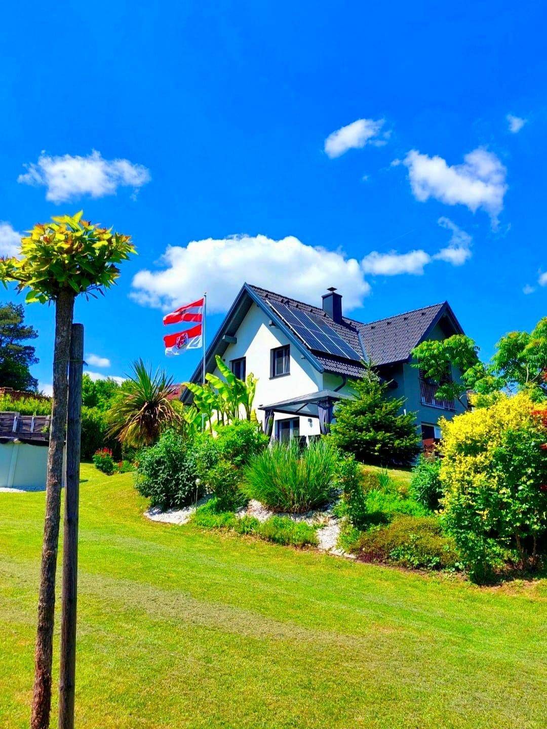 Malerisches Einfamilienhaus umgeben von üppigem Grün und einem weitläufigen Garten unter blauem Himmel.