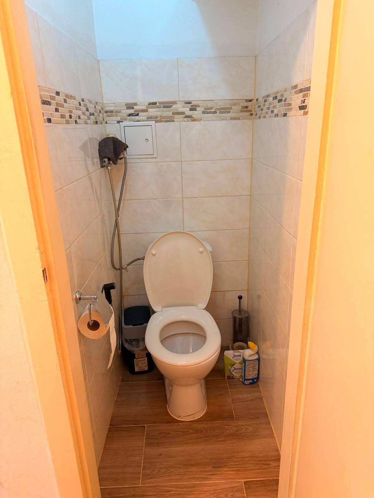 Separates WC mit Toilette und hellen Fliesen an den Wänden.