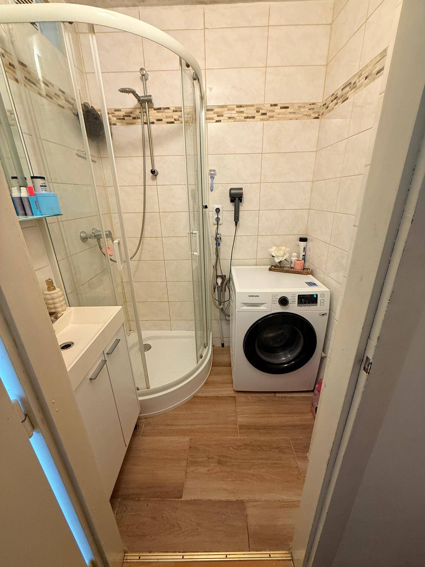 Funktionales Badezimmer mit Eckdusche, Waschbecken und integrierter Waschmaschine.