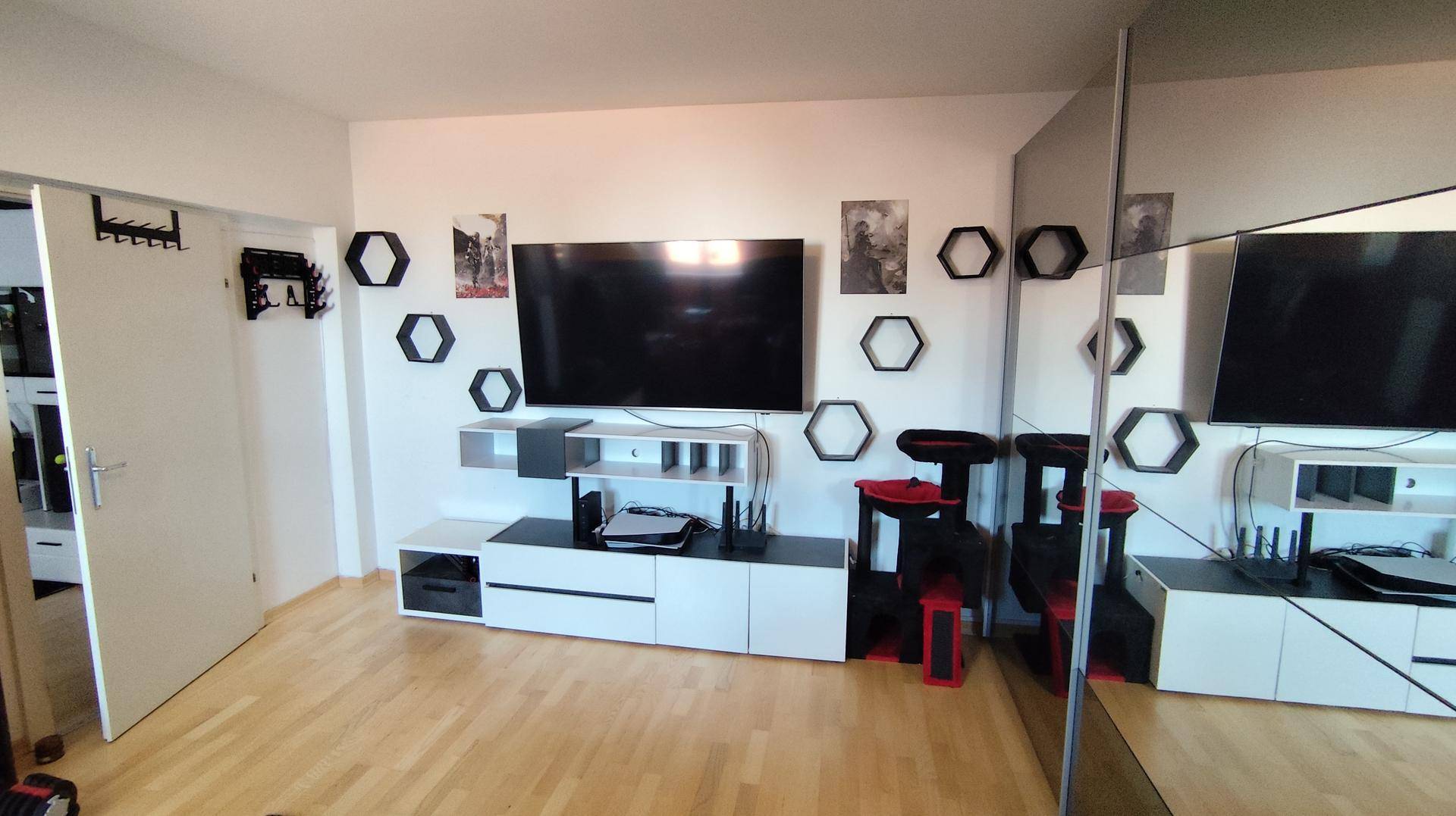 Moderner Wohnbereich mit großem Fernseher, Mediamöbeln, dekorativen Wandregalen und einer Spiegelfront.
