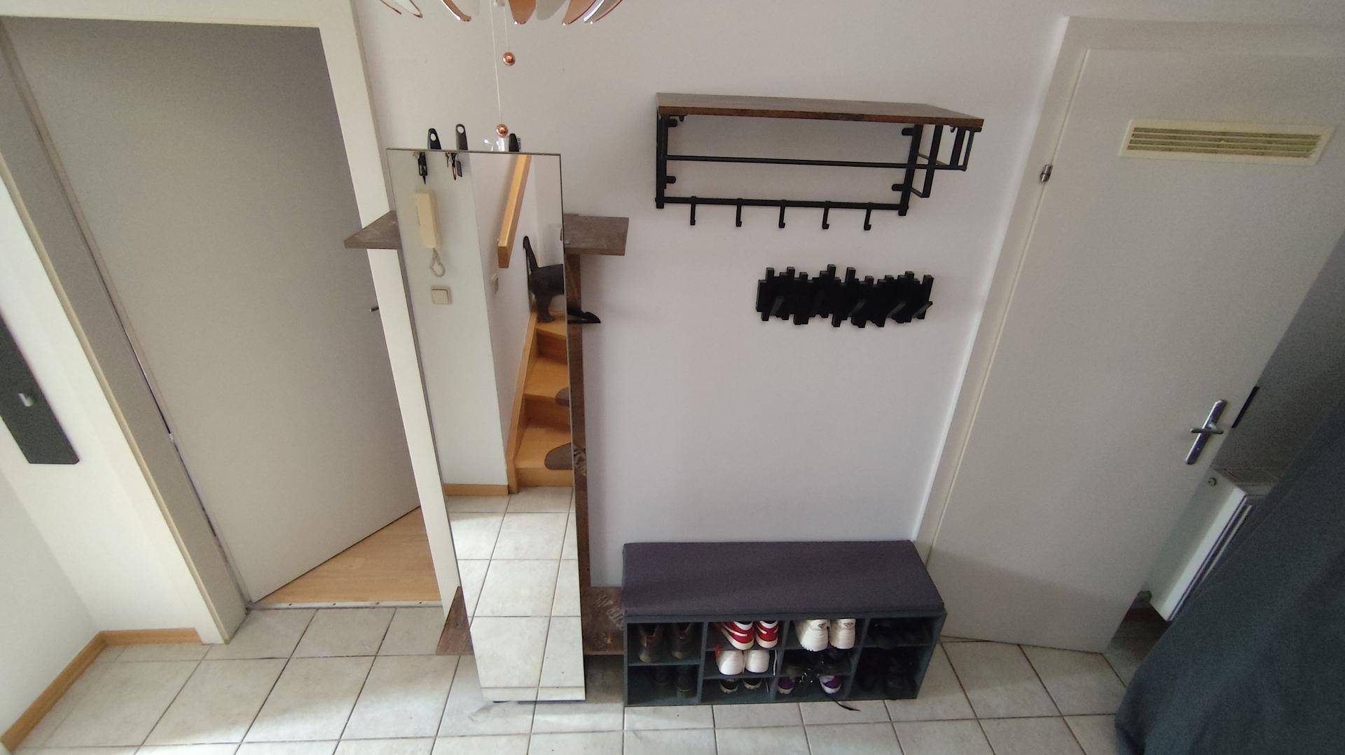 Heller Flur mit großem Spiegel, Schuhbank und Wandgarderobe auf Fliesenboden.