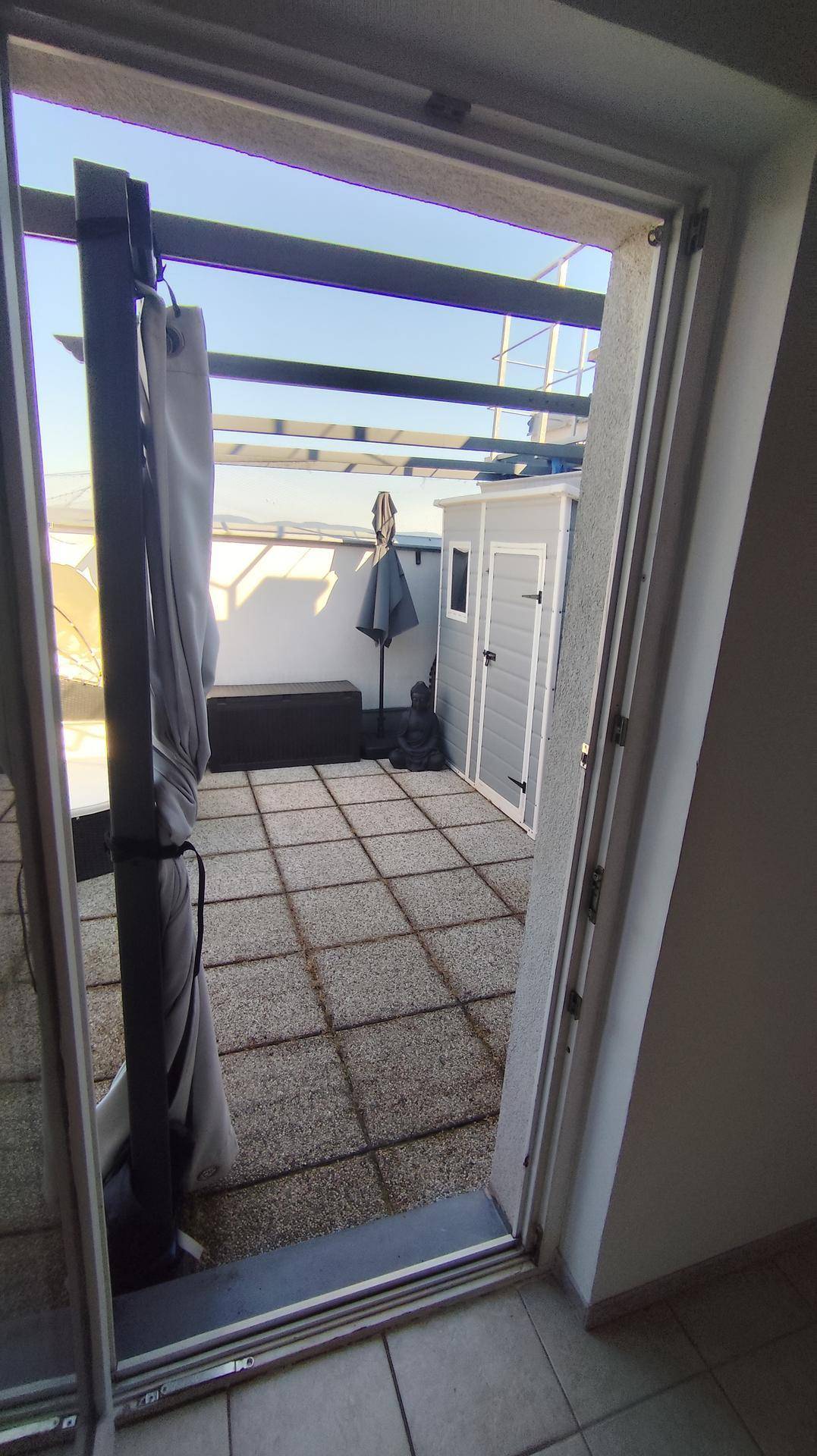 Blick von innen durch die Terrassentür auf die möblierte Dachterrasse mit Stadtpanorama.