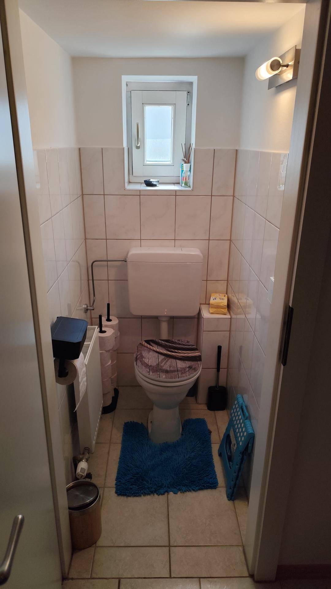Helles Gäste-WC mit weißer Toilette, Fliesen und kleinem Fenster für Tageslicht.