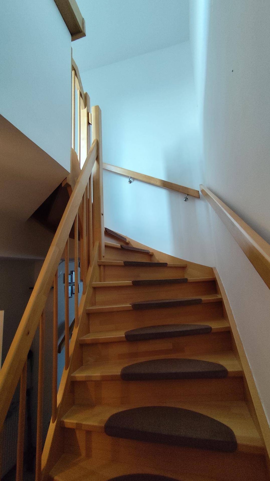 Helle Holztreppe mit Teppichstufen und Holzgeländer, die in die obere Etage führt.