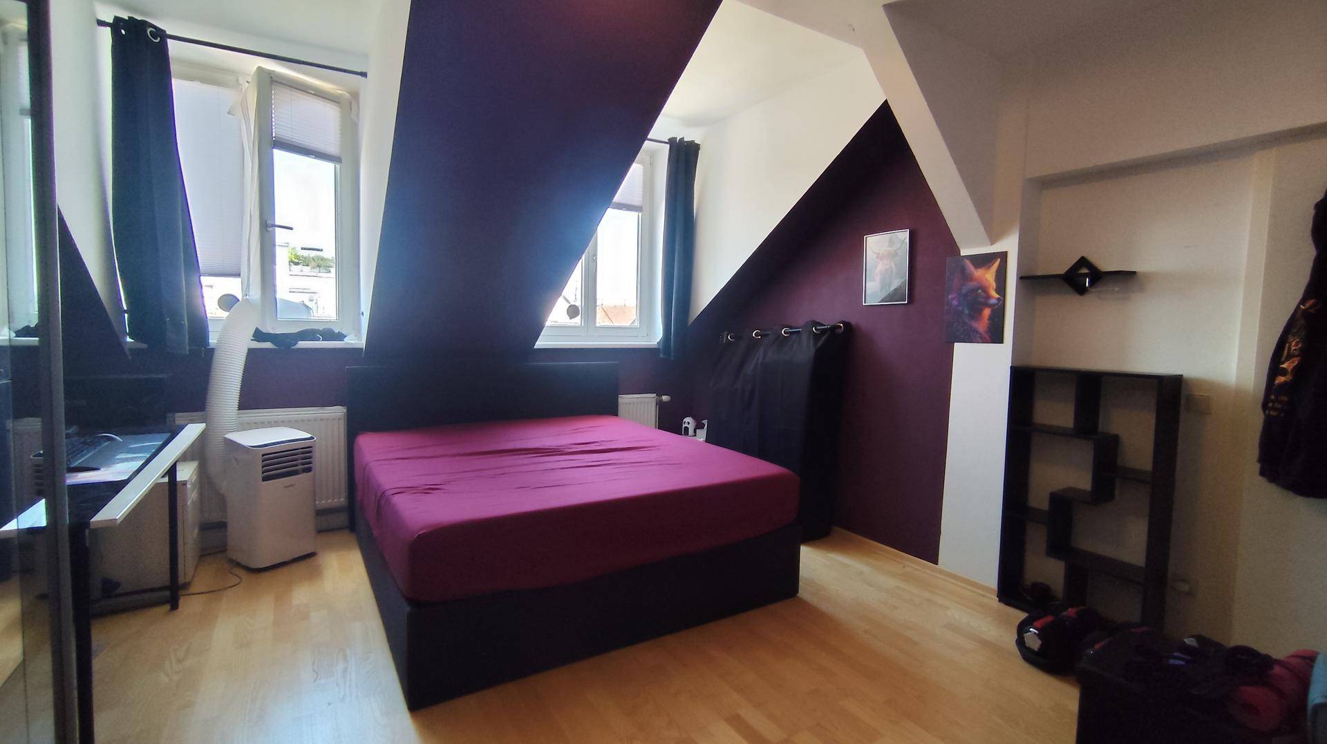 Helles Schlafzimmer mit Dachschrägen, großem Fenster und moderner Einrichtung in Lila- und Weißtönen.