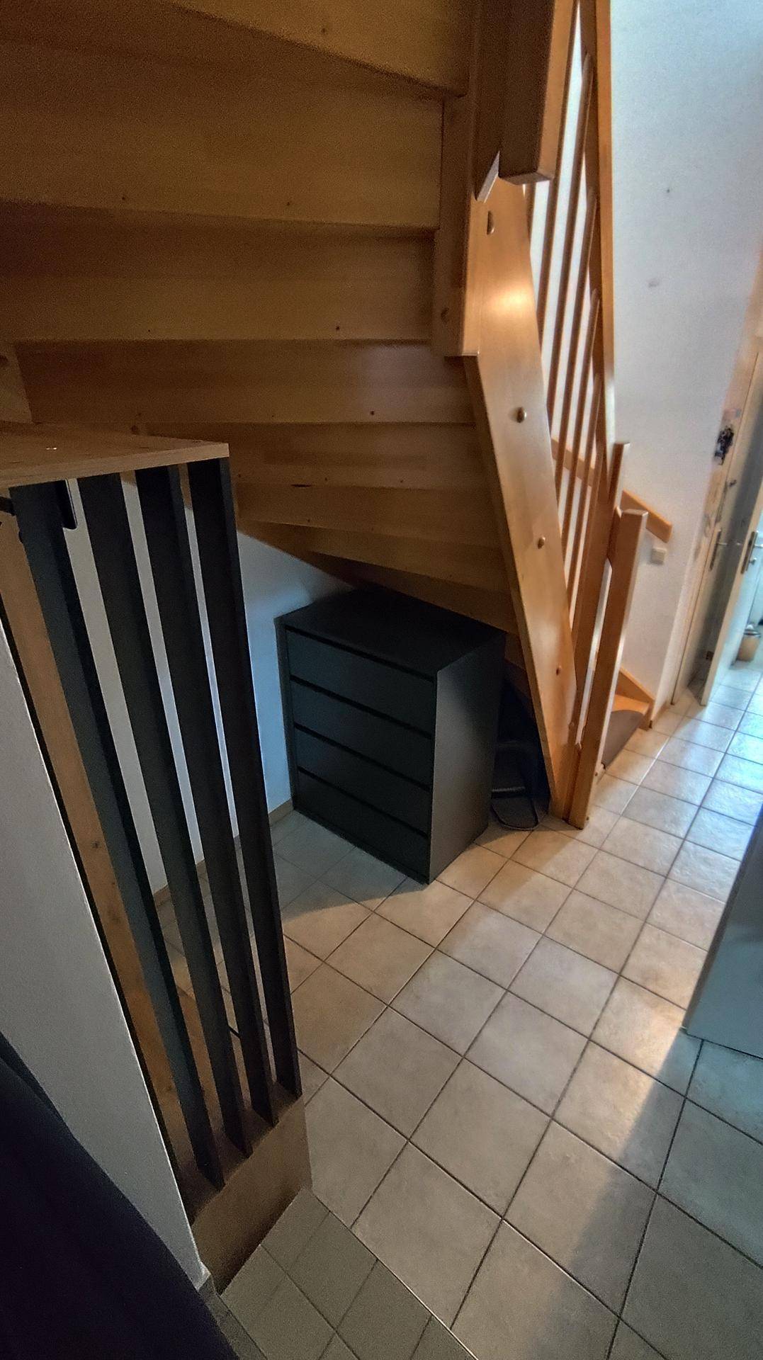 Blick unter die Holztreppe mit einem dunklen Schrank und Fliesenboden im Flurbereich.