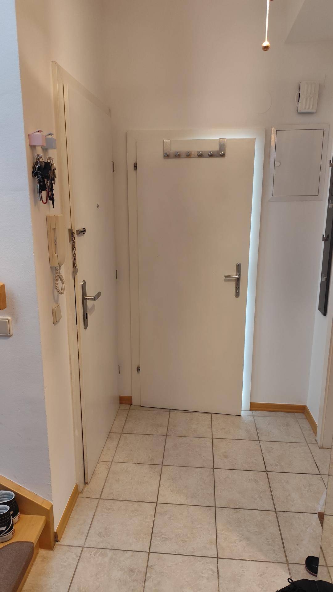 Heller Flur mit mehreren Türen, Fliesenboden und Gegensprechanlage an der Wand.