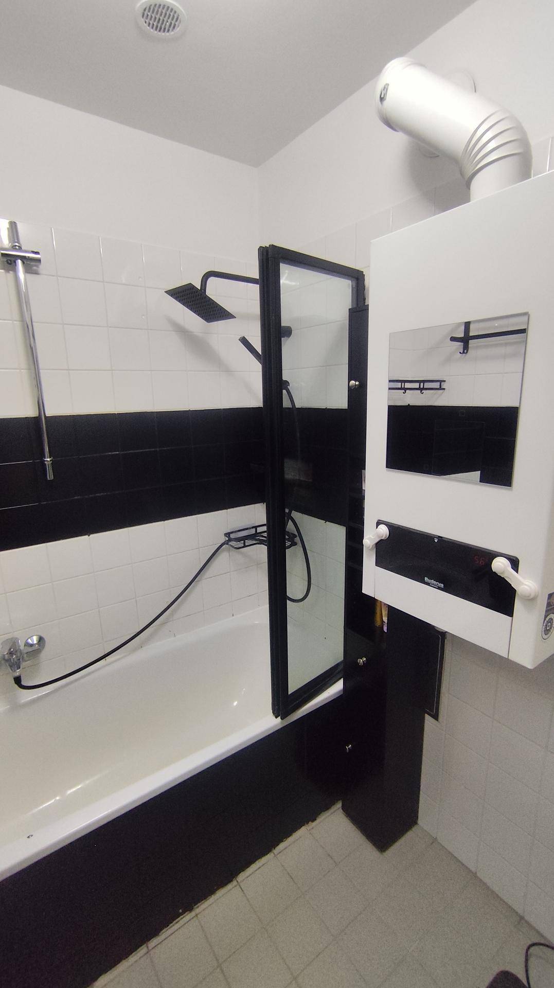 Badezimmer mit Badewanne, Duschabtrennung und schwarz-weißen Wandfliesen.