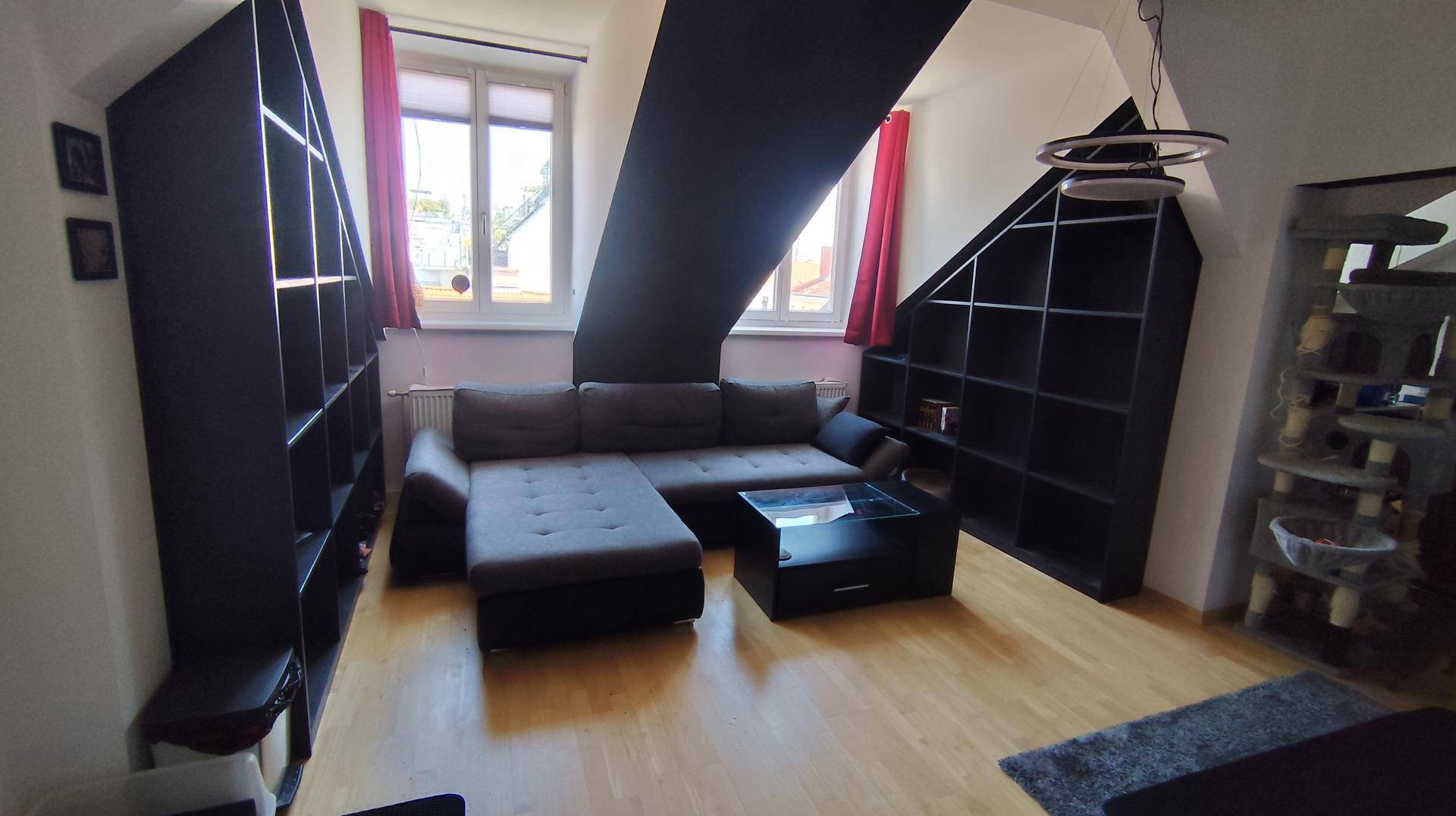 Gemütliches Wohnzimmer mit Ecksofa, Couchtisch und maßgefertigten schwarzen Regalen unter der Dachschräge.