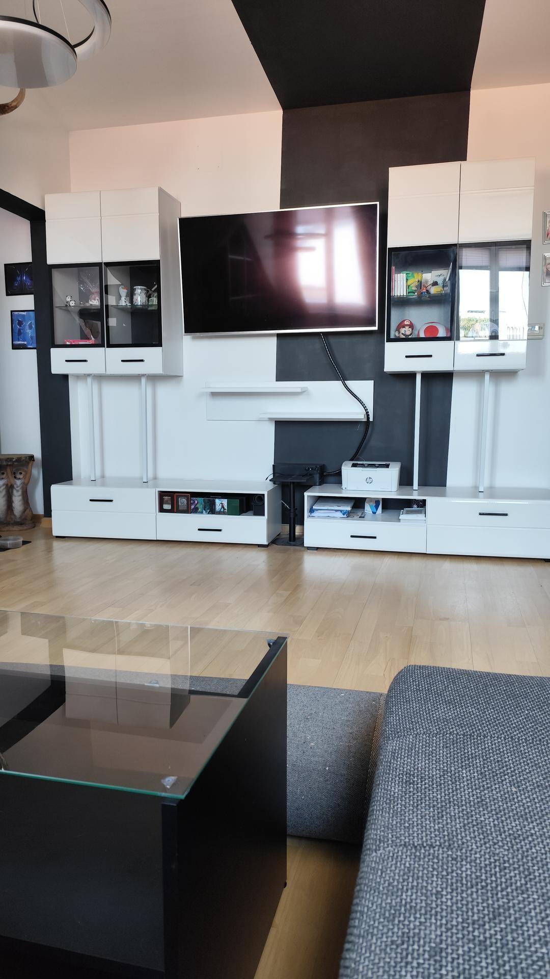 Wohnzimmer mit moderner Medieneinheit, Glastisch und Sofa unter einer auffälligen schwarz-weiß gestreiften Decke.