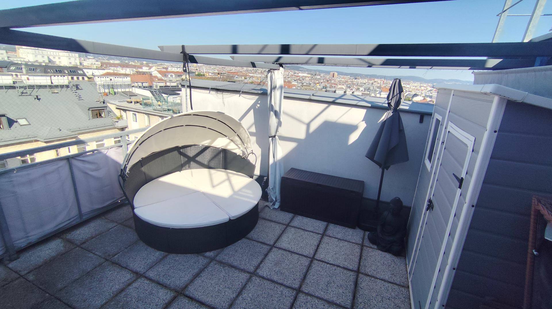 Sonniger Dachterrasse mit bequemer Liege, Gartenhaus und Panoramablick über die Stadt.