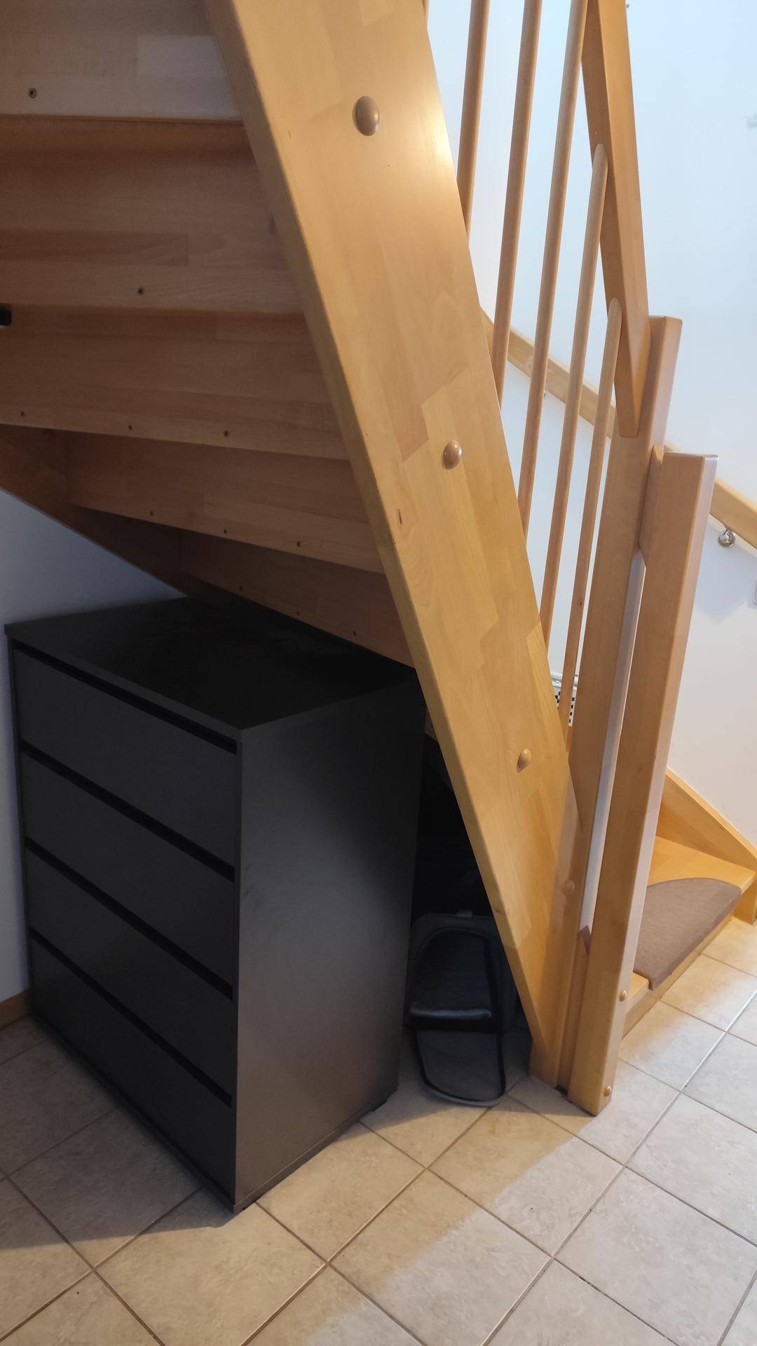 Holztreppe mit dunklem Schrank darunter und Fliesenboden im Eingangsbereich.