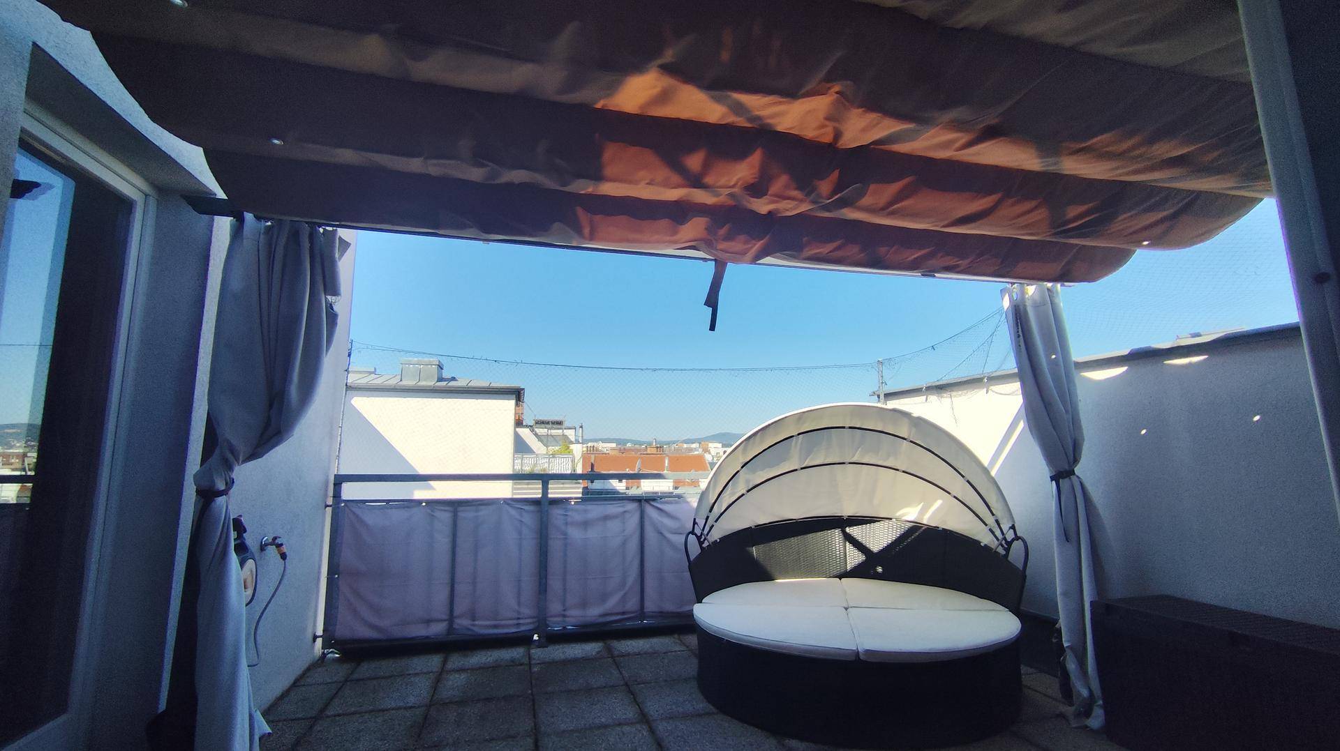 Dachterrasse mit ausgefahrenem Sonnenschutz, Lounge-Möbeln und weitem Stadtblick.