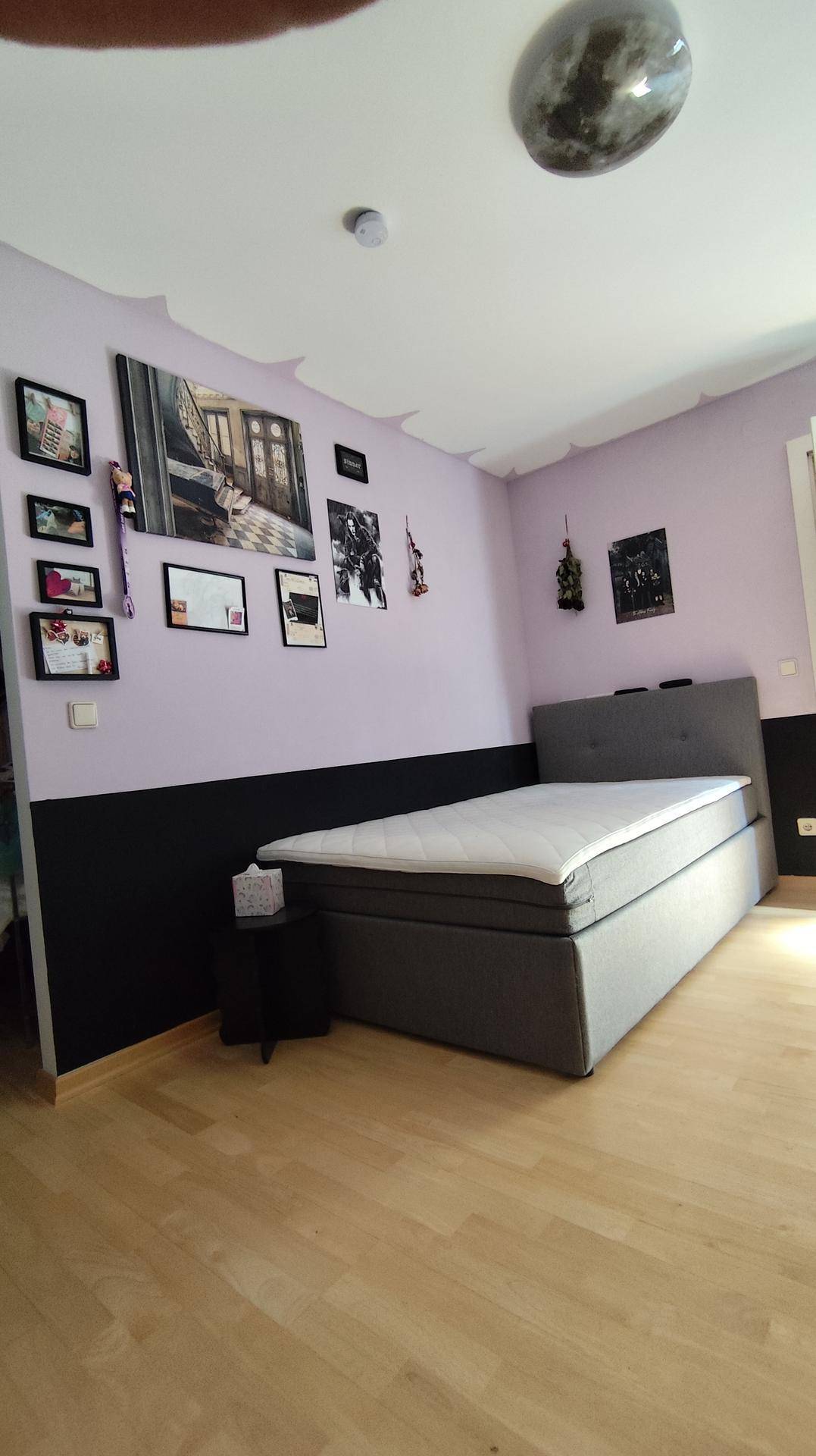 Schlafzimmer mit Boxspringbett, lila und schwarzer Wandgestaltung und einer Vielzahl von Wanddekorationen.
