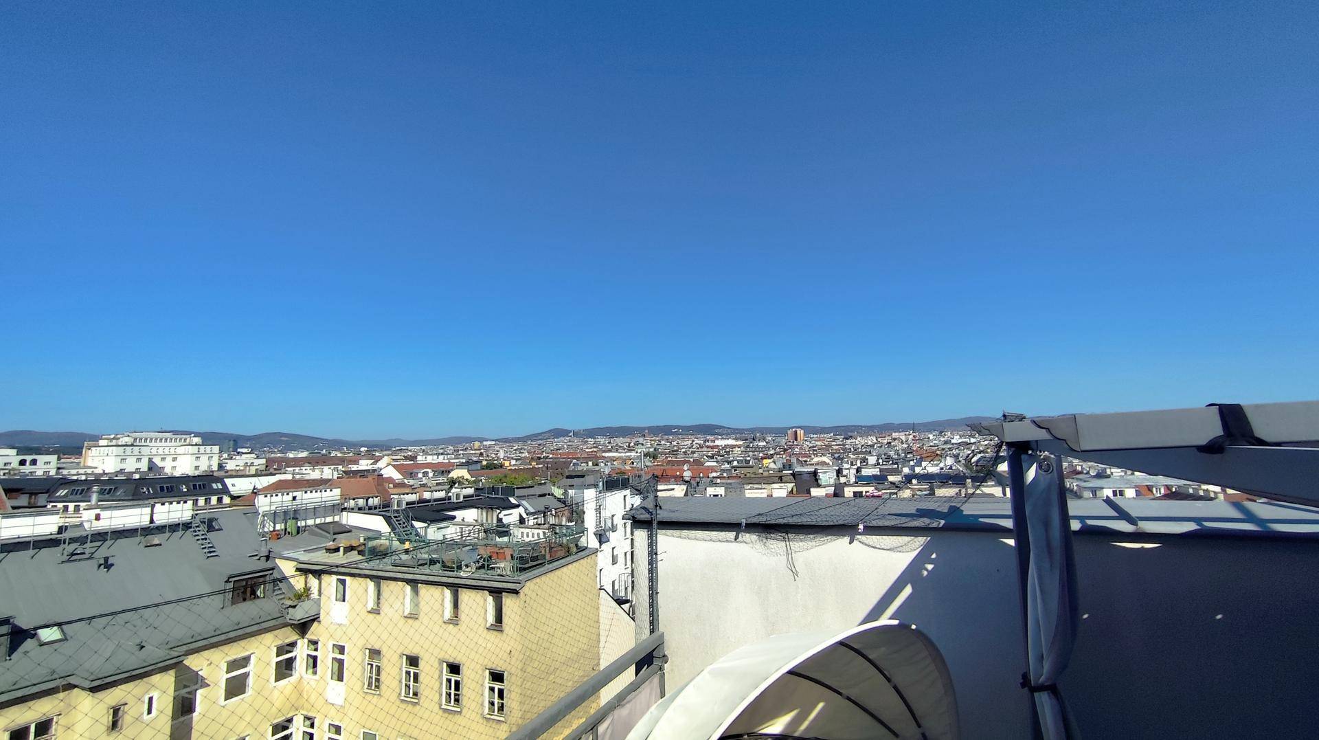 Weitläufiger Blick über die Stadt mit Gebäuden und Bergen am Horizont unter klarem Himmel.