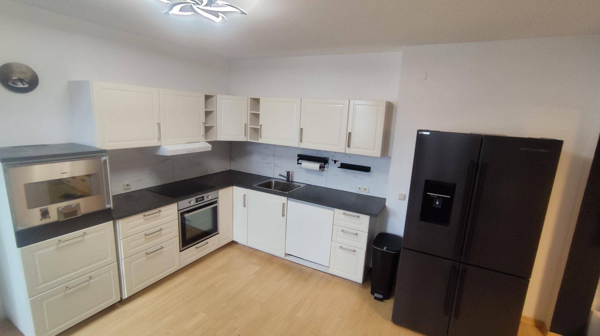 Geräumige Küche mit weißen Schränken, dunklen Arbeitsplatten und großem Kühlschrank.