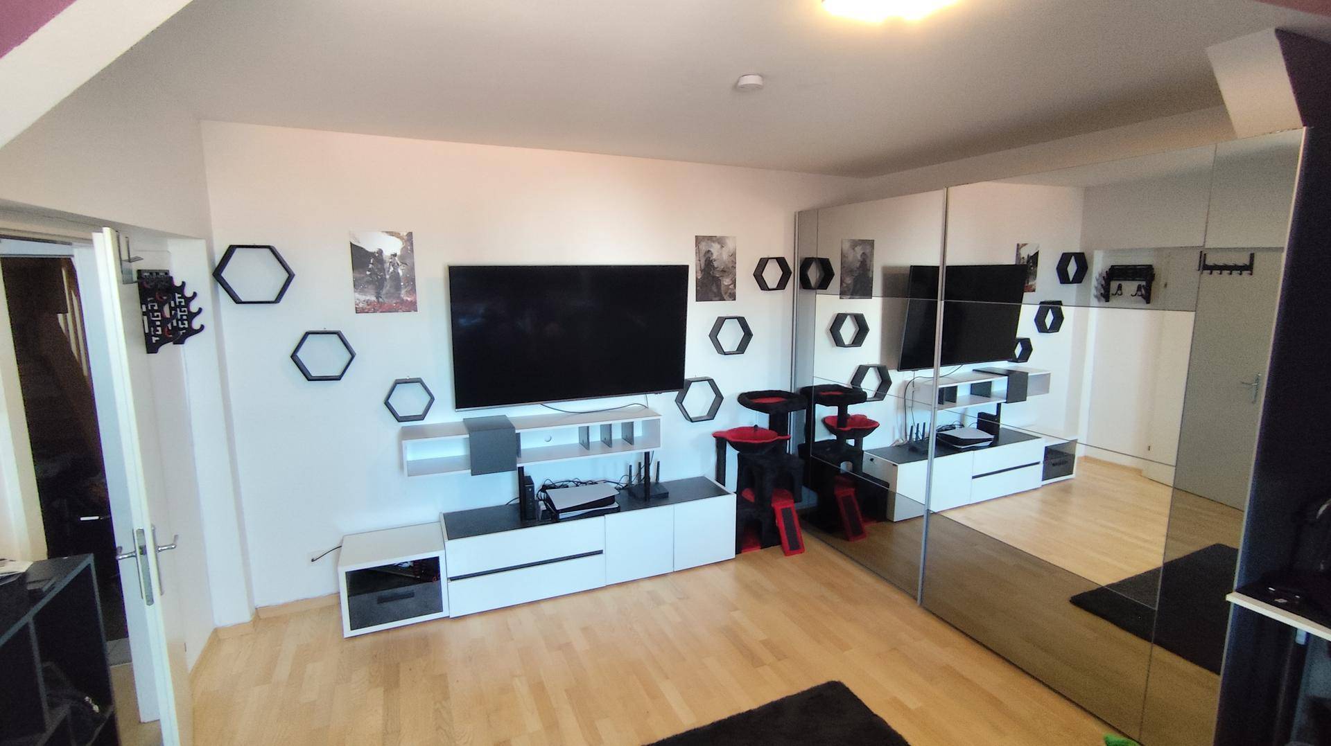 Geräumiger Wohnbereich mit Fernseher, Mediamöbeln und einer großen Spiegelfront, die den Raum optisch erweitert.