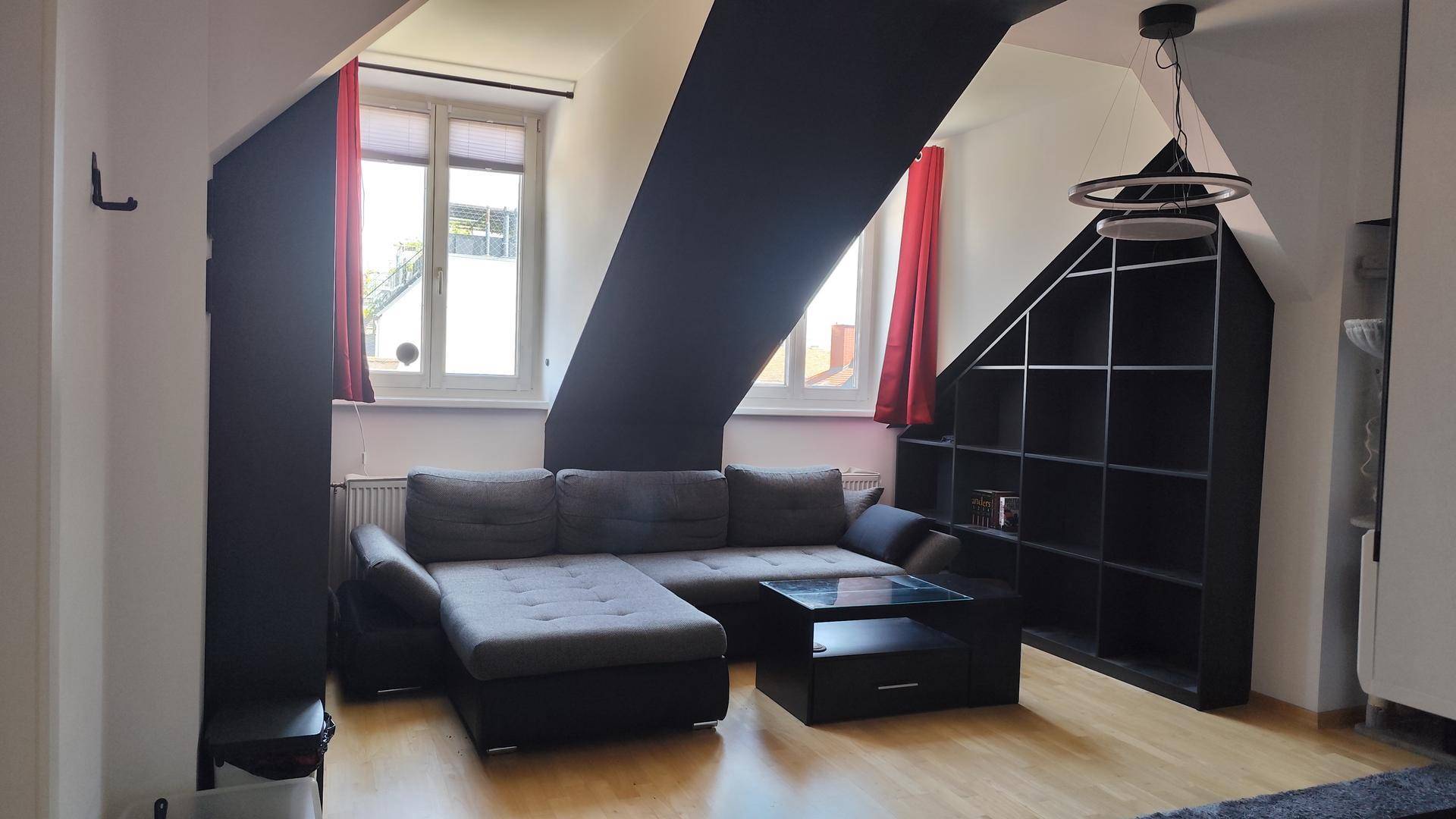 Geräumiges Wohnzimmer mit Dachschrägen, großen Fenstern und praktischen, in die Schräge integrierten Regalen.