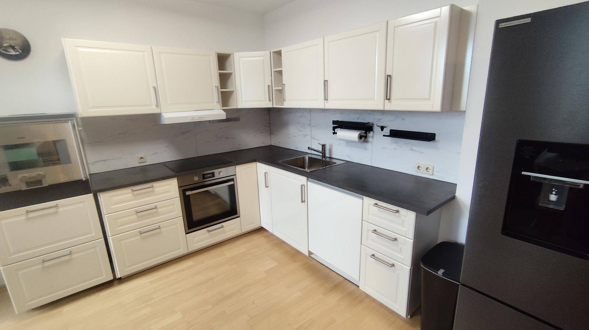 Moderne Küche mit weißen Schränken, dunklen Arbeitsplatten und integriertem Backofen.