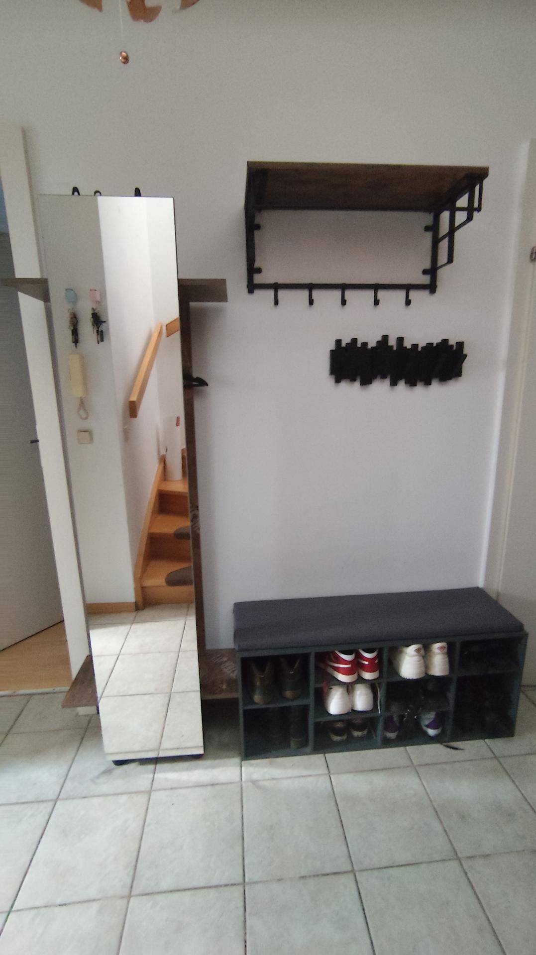 Geräumiger Flur mit Spiegel, Schuhbank und Wandgarderobe auf hellen Fliesen.