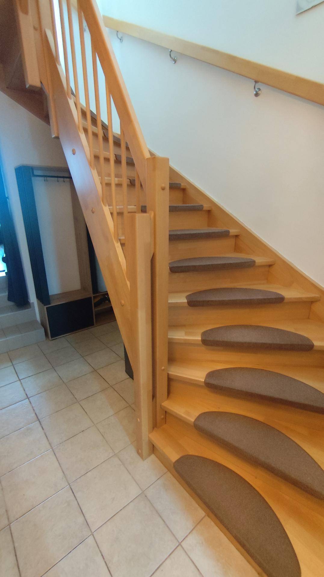 Helle Holztreppe mit Teppichstufen und Fliesenboden im Eingangsbereich des Hauses.