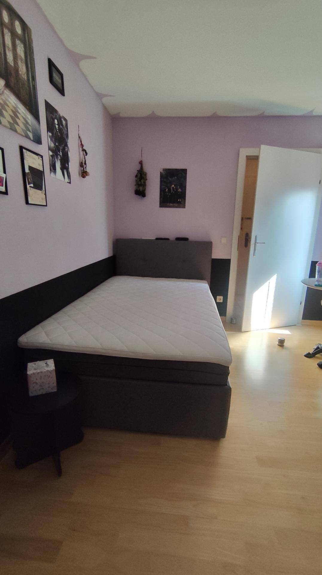 Schlafzimmer mit Boxspringbett, lila und schwarzer Wandgestaltung und einer Sammlung gerahmter Bilder.