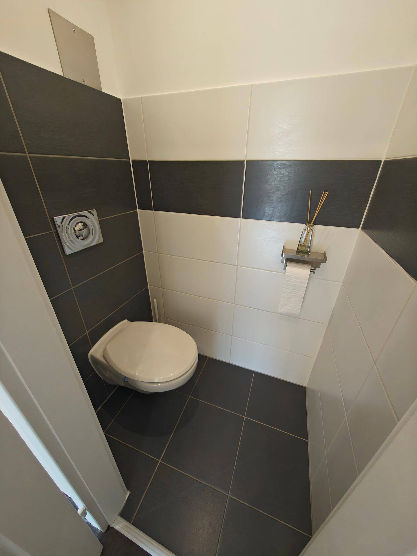 Gäste-WC mit wandhängender Toilette und modernen Fliesen in Weiß und Dunkelgrau.