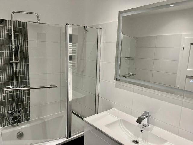 Badewanne mit Duschwand und modern gefliesten Wänden in Weiß und Dunkelgrau.