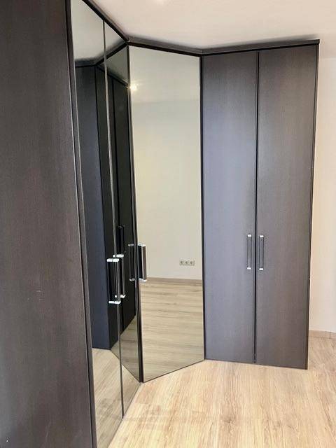 Schlafzimmer mit hellem Laminatboden und einem Eckkleiderschrank mit Spiegeltüren.