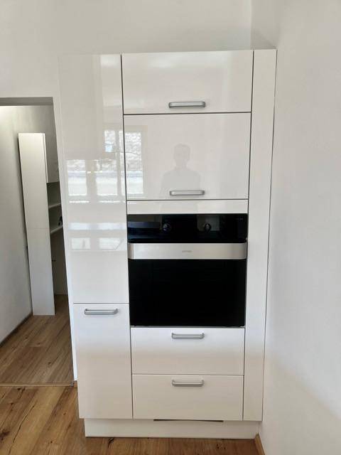 Hoher Küchenschrank mit integriertem Backofen und glänzenden weißen Fronten.