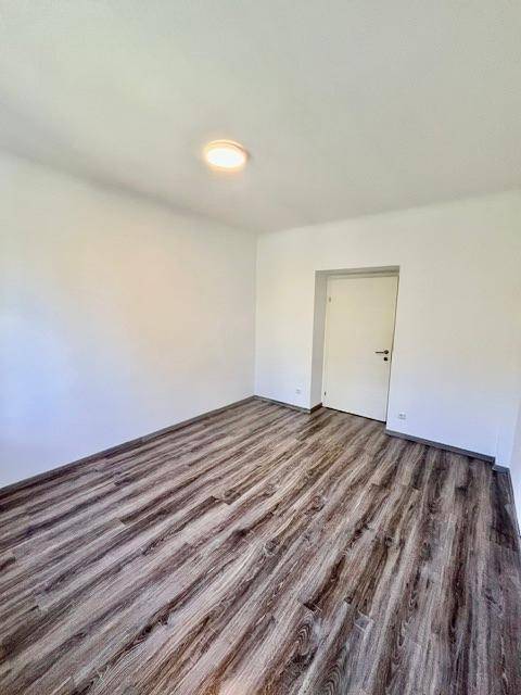 Schlafzimmer mit dunklem Laminatboden und weiß gestrichenen Wänden.
