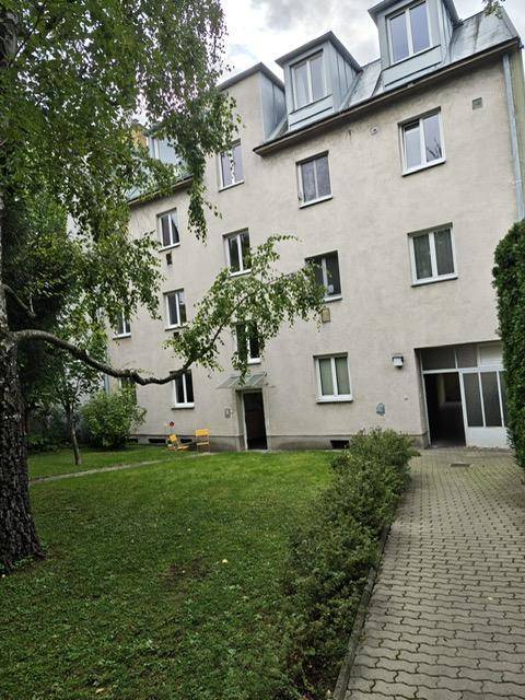 Seitenansicht des Gebäudes mit gepflastertem Weg und Grünfläche.