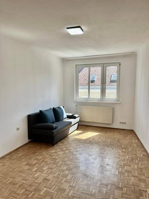 Gemütlicher Raum mit Parkettboden, Fenster und einem dunklen Sofa, ideal als Wohnzimmer.