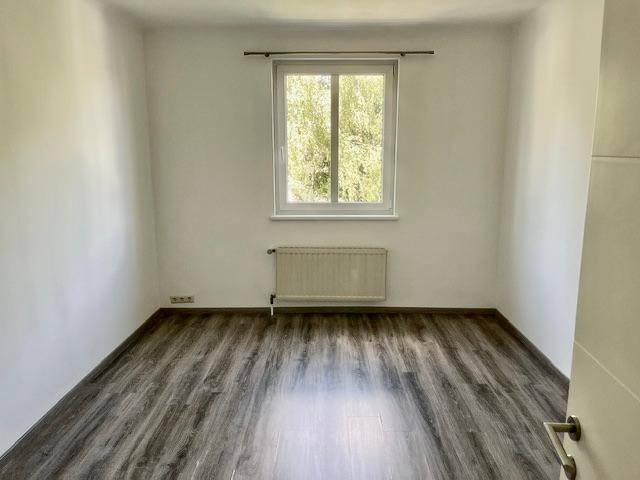 Schlafzimmer mit dunklem Laminatboden, weißen Wänden und Blick ins Grüne.