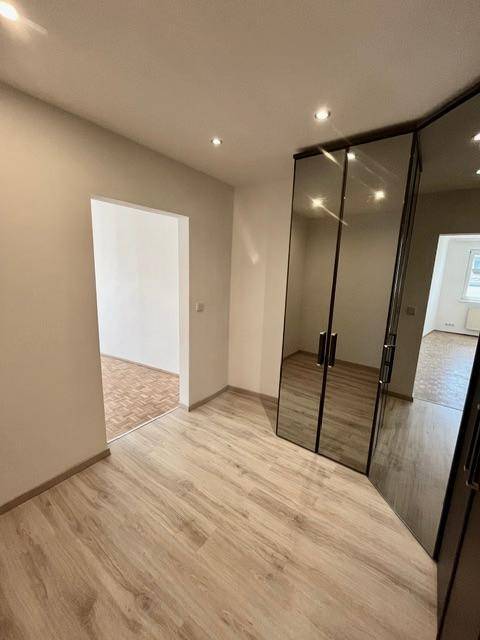 Schlafzimmer mit Spiegelschrank und Zugang zu einem weiteren Raum, auf hellem Laminatboden.